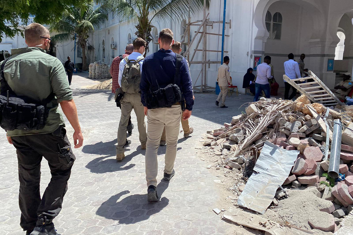 Livvakter med ryggsäckar syns gå förbi en hög med bråte och i bakgrunden syns palmer.